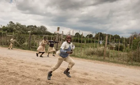 A person running across a sandy field with others behind.