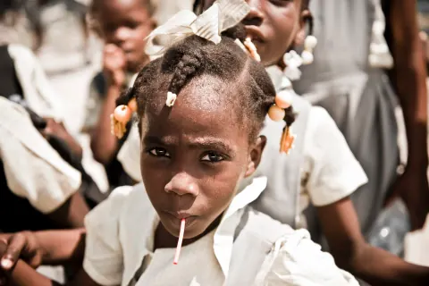 A schoolgirl with braided hair and white ribbons looking at the camera.