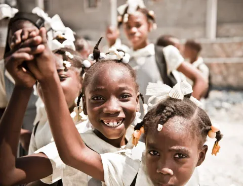 Smiling schoolchildren raising their hands toward the camera.