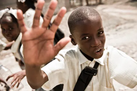 A schoolboy holding an open hand toward the camera.