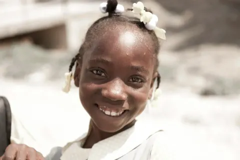 A smiling schoolgirl with white ribbons in her hair.