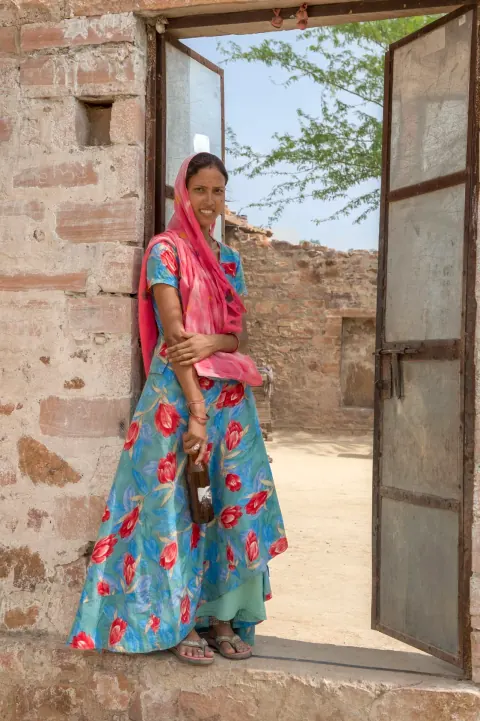 A woman in brightly coloured clothing standing in an open doorway.
