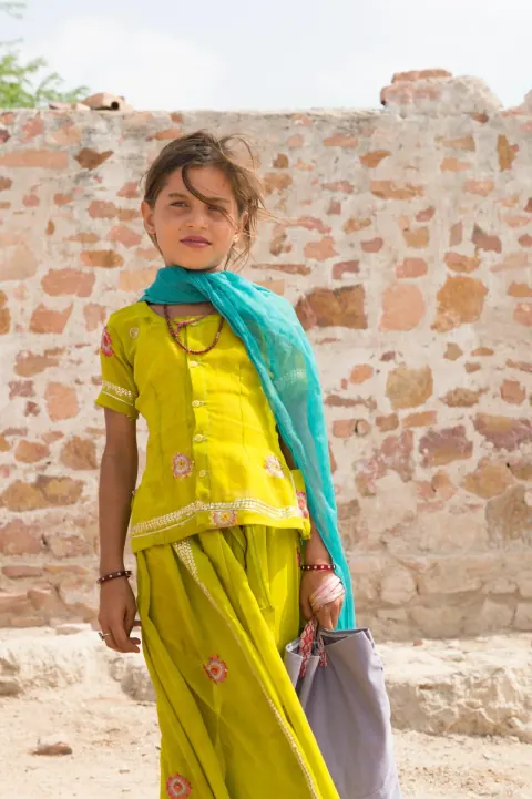 A girl in yellow clothing and a blue-green scarf against a stone wall.
