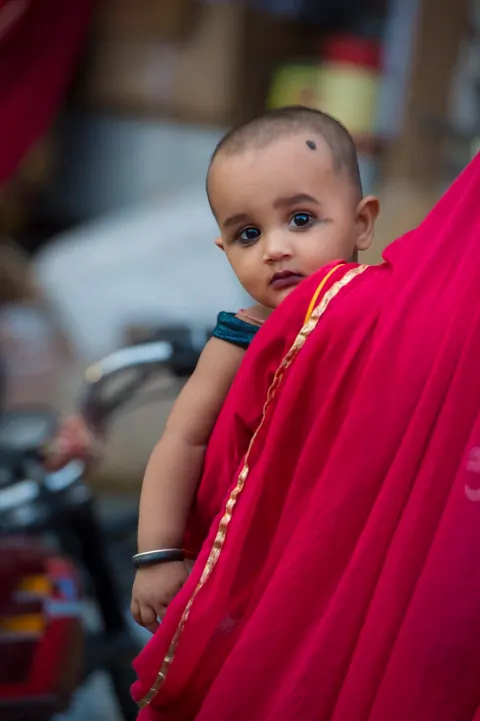 A baby looking over the shoulder of someone in bright pink clothing.