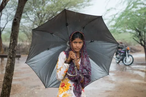 A girl holding an open umbrella on a tree-lined path.