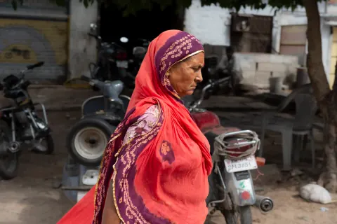 A woman in a red scarf walking past parked motorcycles.