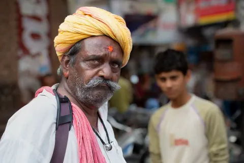 A bearded man in a yellow turban and pink scarf on a busy street.