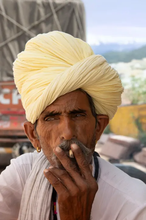 A man in a pale yellow turban holding one hand near his face.