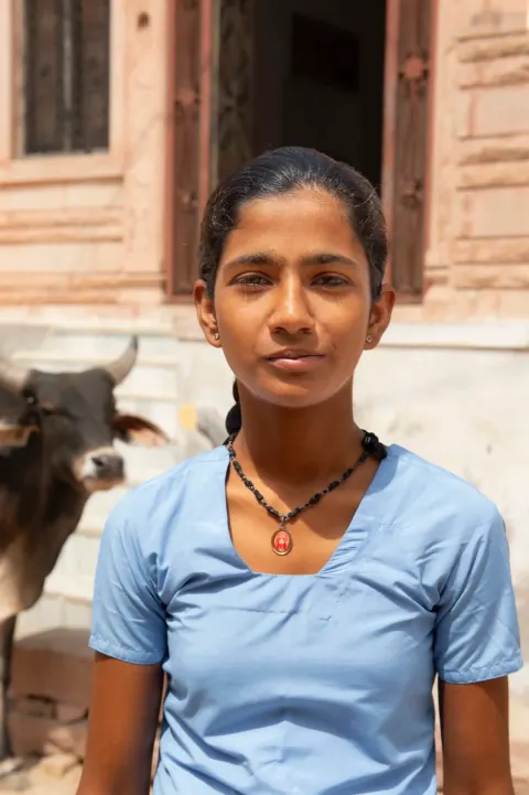 A young woman in a blue top standing on a sunlit street.