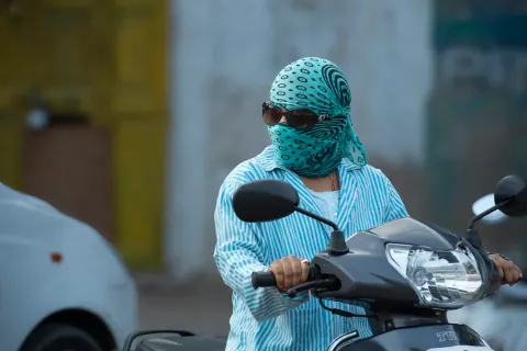 A scooter rider with a turquoise patterned scarf covering their face.