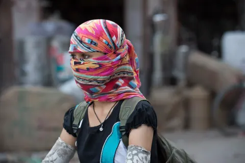 A person with a multicoloured scarf wrapped around their head and face.