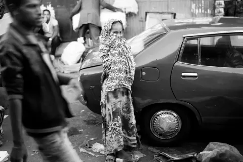 A black-and-white street scene with a woman beside a parked car.