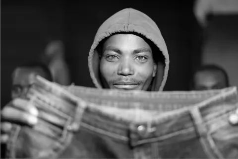 A black-and-white portrait of a hooded man looking over an open newspaper.