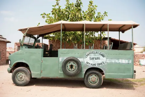 A green open-sided safari vehicle parked beside a brick wall.