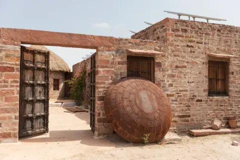 A large round woven object leaning against a brick building.
